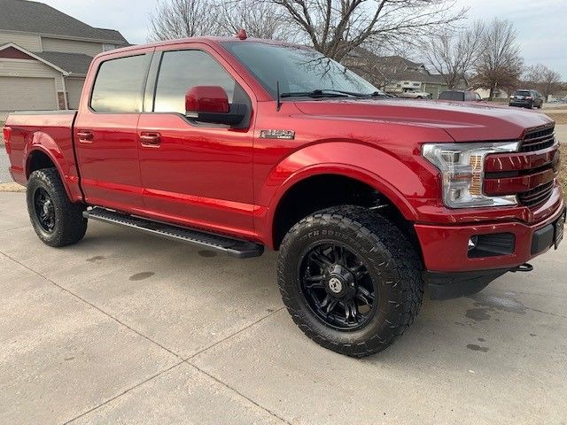 A red ford f150 truck is parked in a driveway in front of a house.