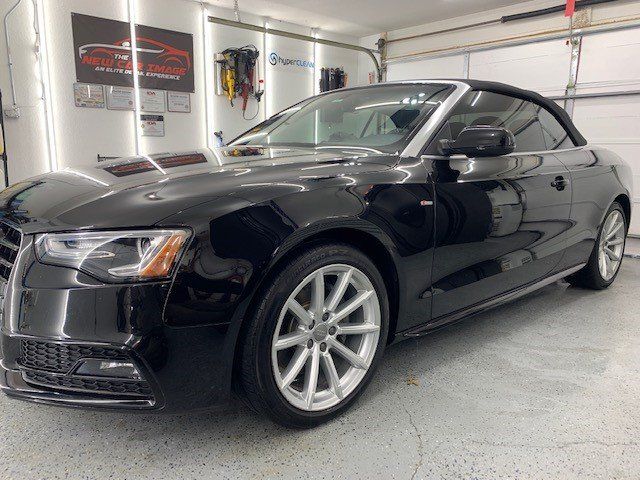 A black audi a5 convertible is parked in a garage.