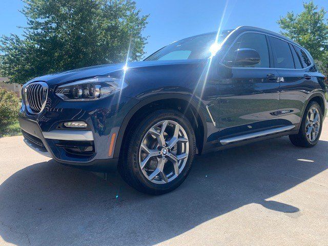 A blue bmw x3 is parked in a driveway on a sunny day.