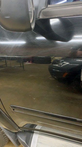 A close up of a car door with a reflection of a car in it.