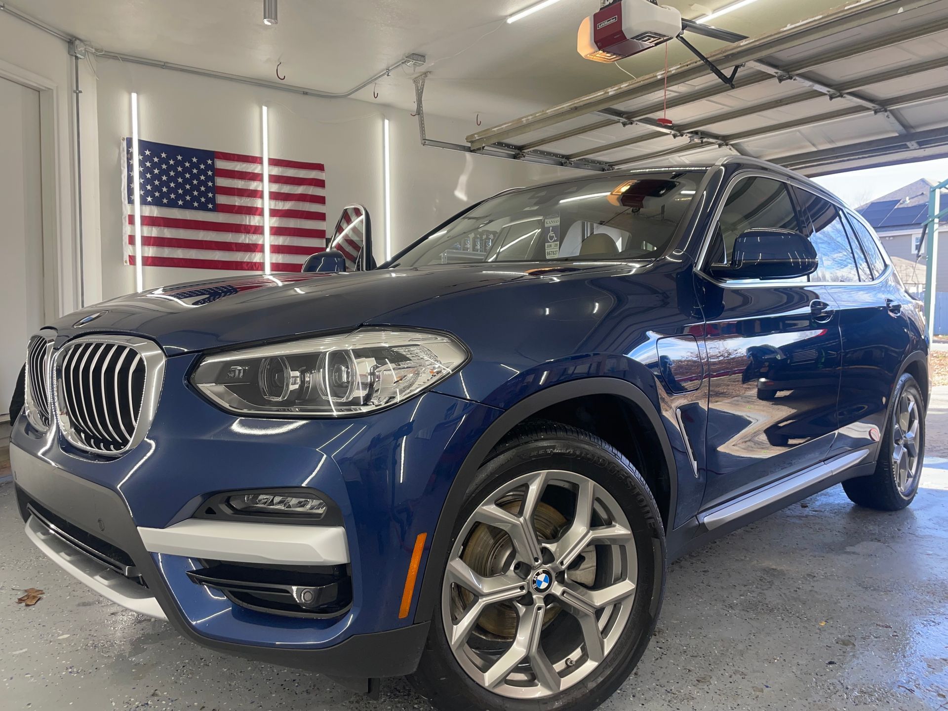 A blue bmw x3 is parked in a garage next to an american flag.