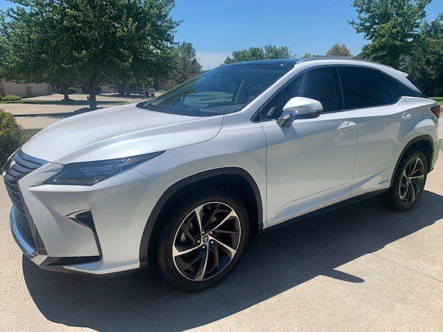 A white lexus is parked in a driveway with trees in the background