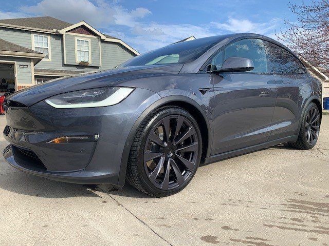 A tesla model x is parked in a driveway in front of a house.