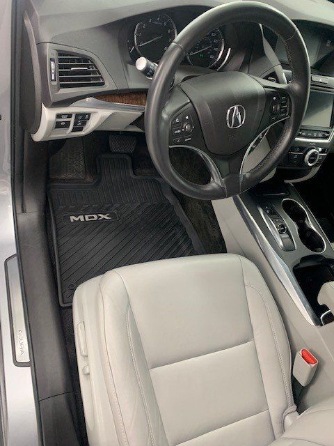 The interior of a silver acura mdx with white leather seats and a black steering wheel.
