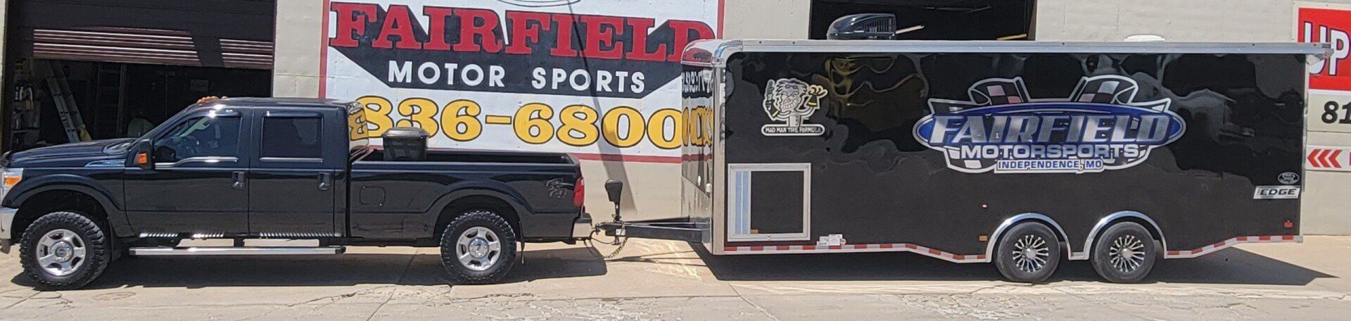 A truck and trailer are parked in front of a sign for fairfield motor sports