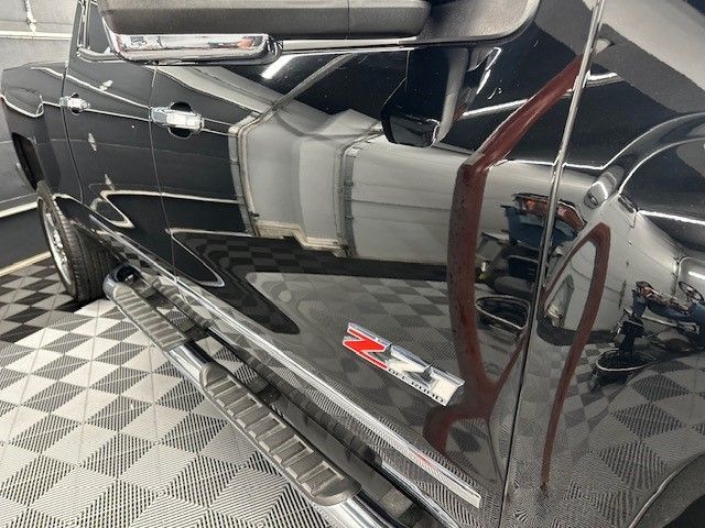 A black truck is parked on a checkered floor in a showroom.