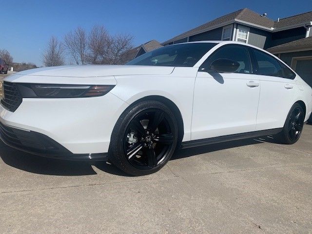 A white car with black wheels is parked in front of a house.