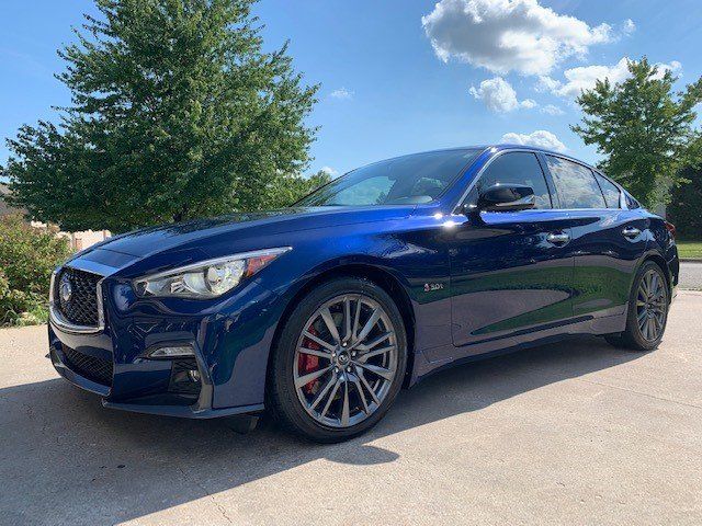 A blue car is parked in a driveway with trees in the background.