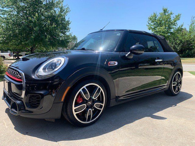 A black mini cooper is parked in a driveway on a sunny day.
