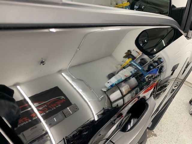 A car is sitting in a garage with a reflection of the car in the mirror.