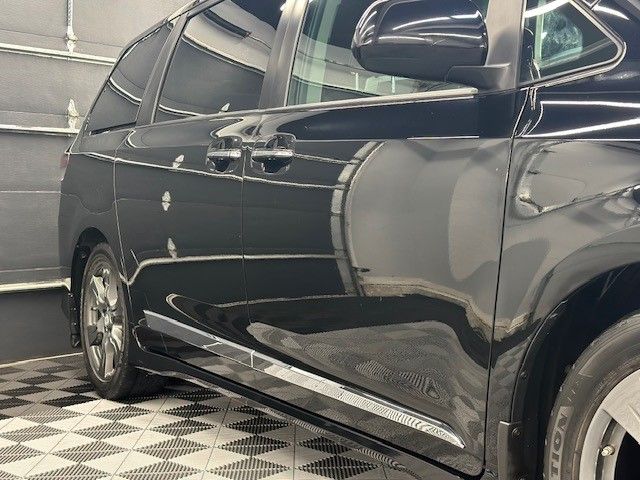 A black minivan is parked on a checkered floor in a garage.