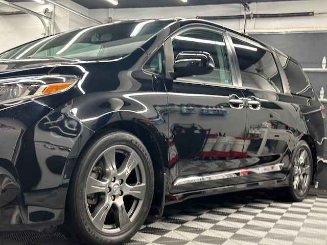 A black minivan is parked in a garage on a checkered floor.