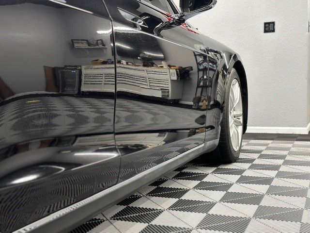 A black car is parked on a checkered floor in a garage.