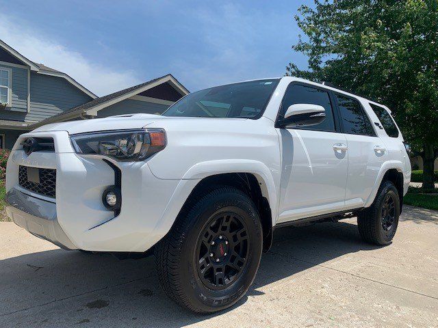 A white toyota 4runner is parked on the side of the road in front of a house.
