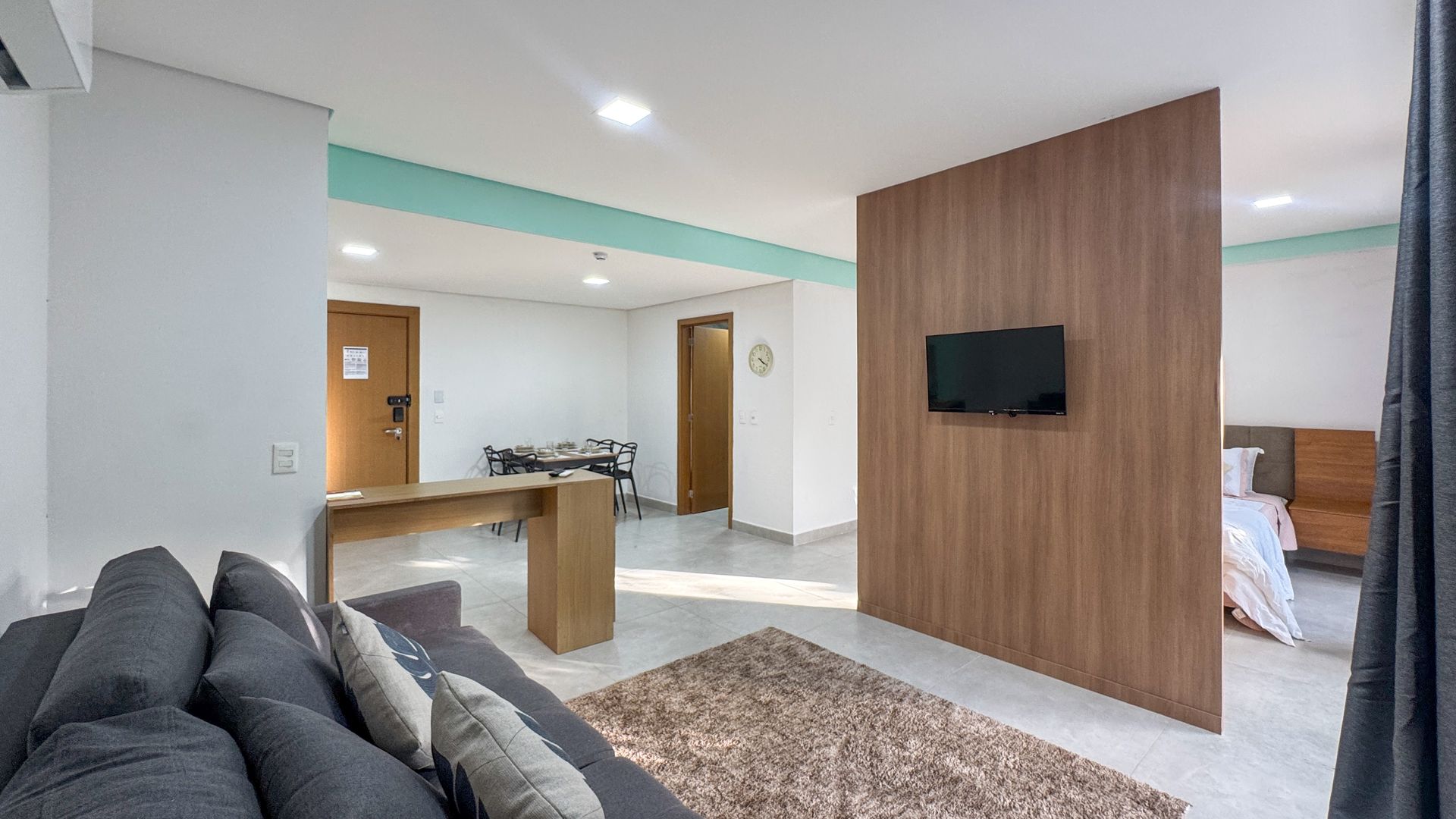 Interior de apartamento estúdio moderno com parede de destaque em madeira, sofá e TV.