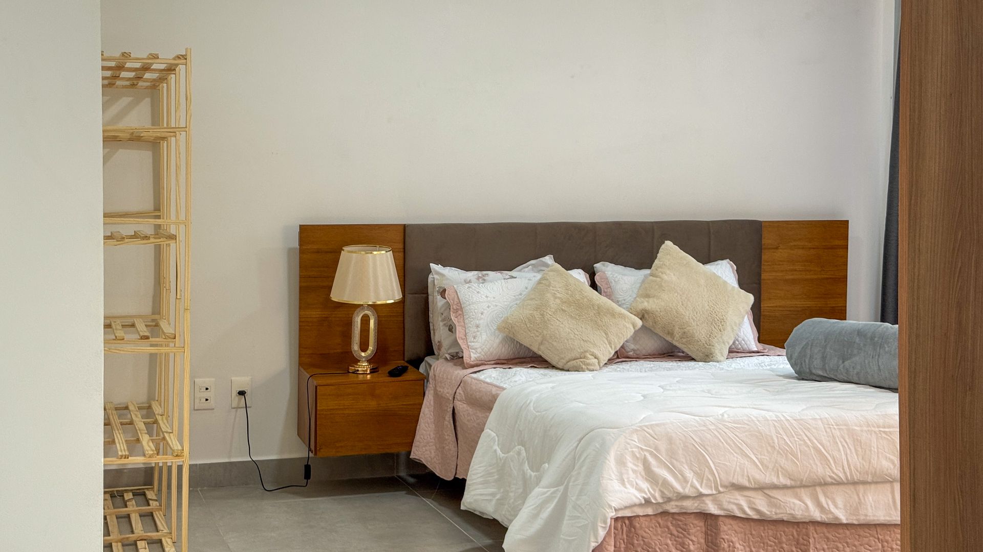 Quarto com cama, mesa de cabeceira, abajur e estante.