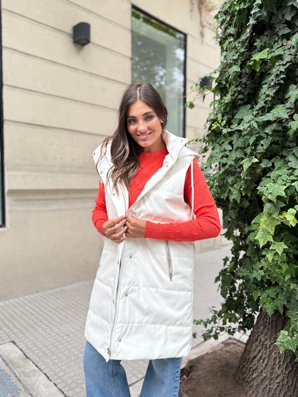 Una mujer que lleva un chaleco blanco y un suéter rojo está parada frente a un edificio.