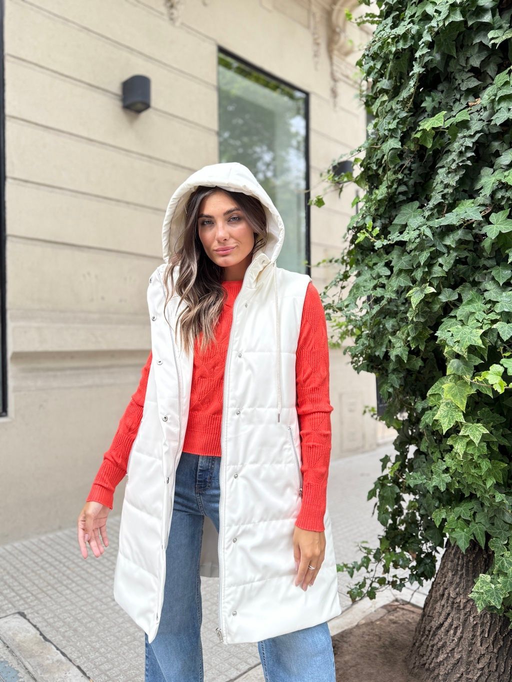 Una mujer que lleva un chaleco blanco y un suéter rojo está parada frente a un edificio.