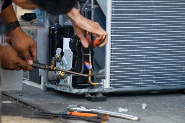 A man is fixing an air conditioner with a wrench.