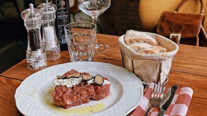 Tartare di manzo con tartufi su un piatto, cestino di pane, bicchiere d'acqua, sale, pepe e sacchetto.