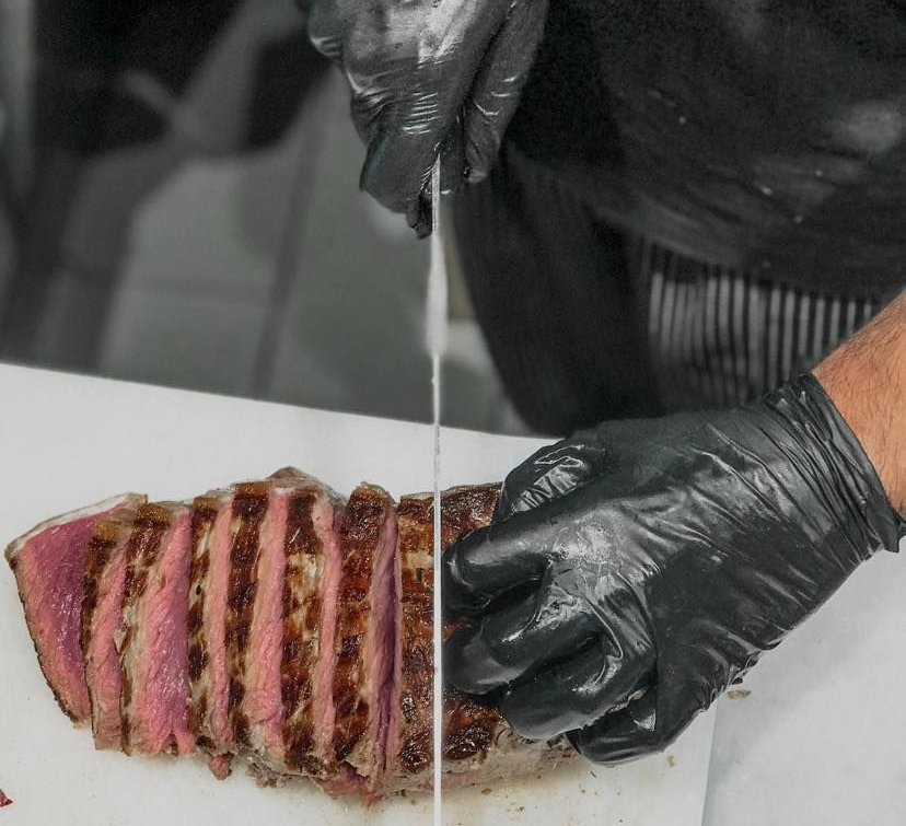 Bistecca tagliata a fette e succosa con patate arrosto ed erbe aromatiche, servita su un piatto di metallo.