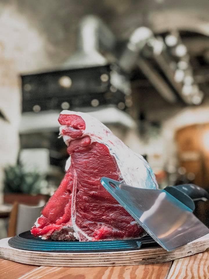 Una persona che regge un vassoio di legno con quattro porzioni di tartare di manzo guarnite con vari contorni.