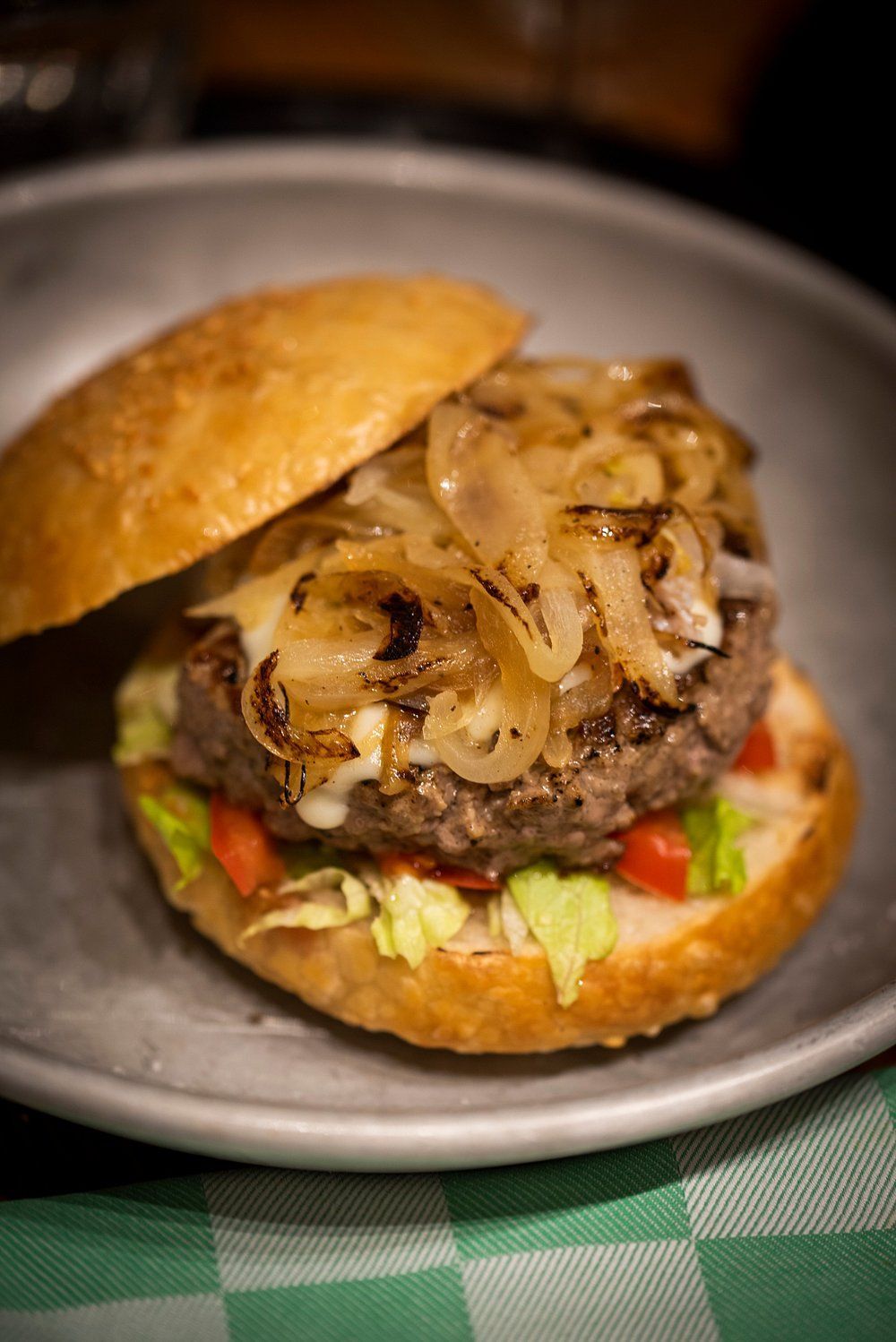 Hamburger con cipolle caramellate e condimenti su un panino, servito in una ciotola di metallo.