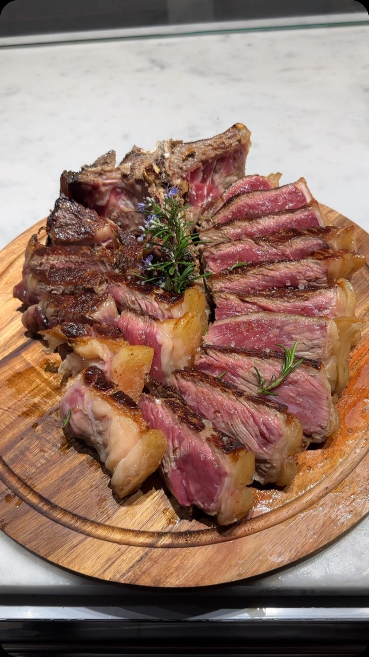 Bistecca tagliata a fette e scottata su un tagliere di legno, al sangue, con erbe aromatiche.