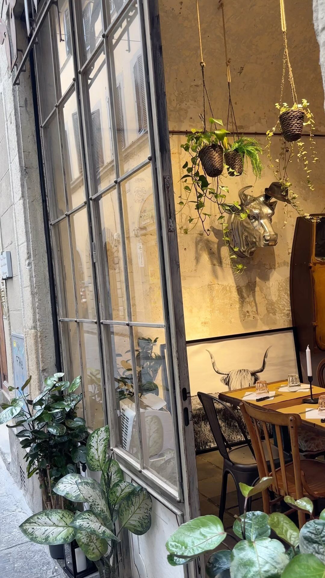 Esterno del ristorante con ampie finestre, piante e vista sui tavoli e sulle decorazioni interne.