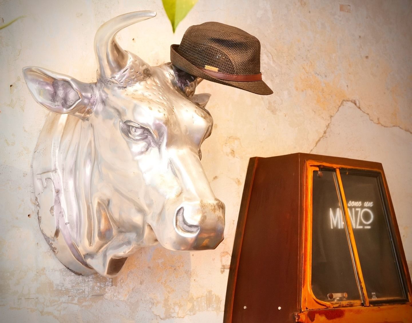 Scultura in argento raffigurante una testa di mucca con cappello; accanto a un jukebox arancione con la scritta 