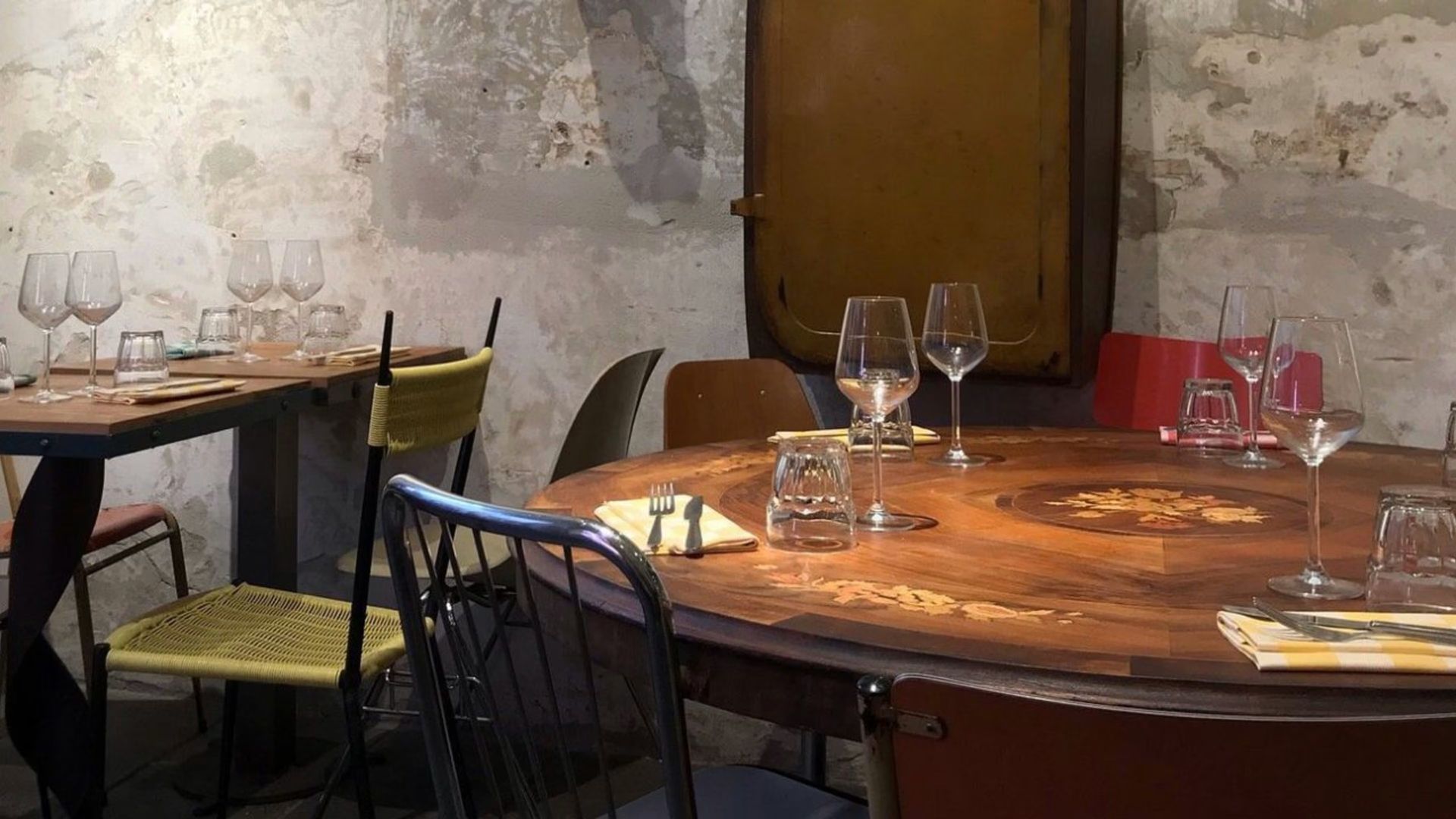 Interno del ristorante: tavoli apparecchiati con bicchieri e posate, sedie spaiate contro pareti in pietra antica.