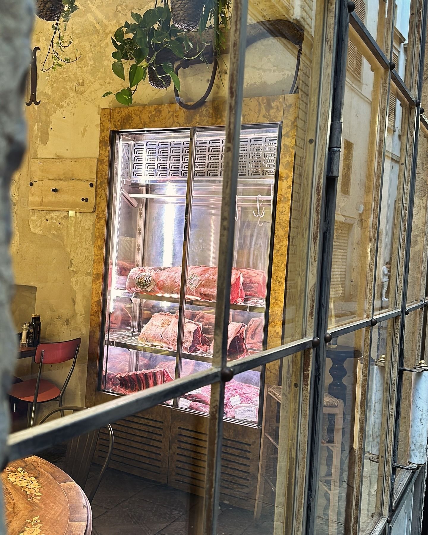 Vetrina per la carne in un edificio in pietra, visibile attraverso un cancello metallico. Si vede la carne rossa.