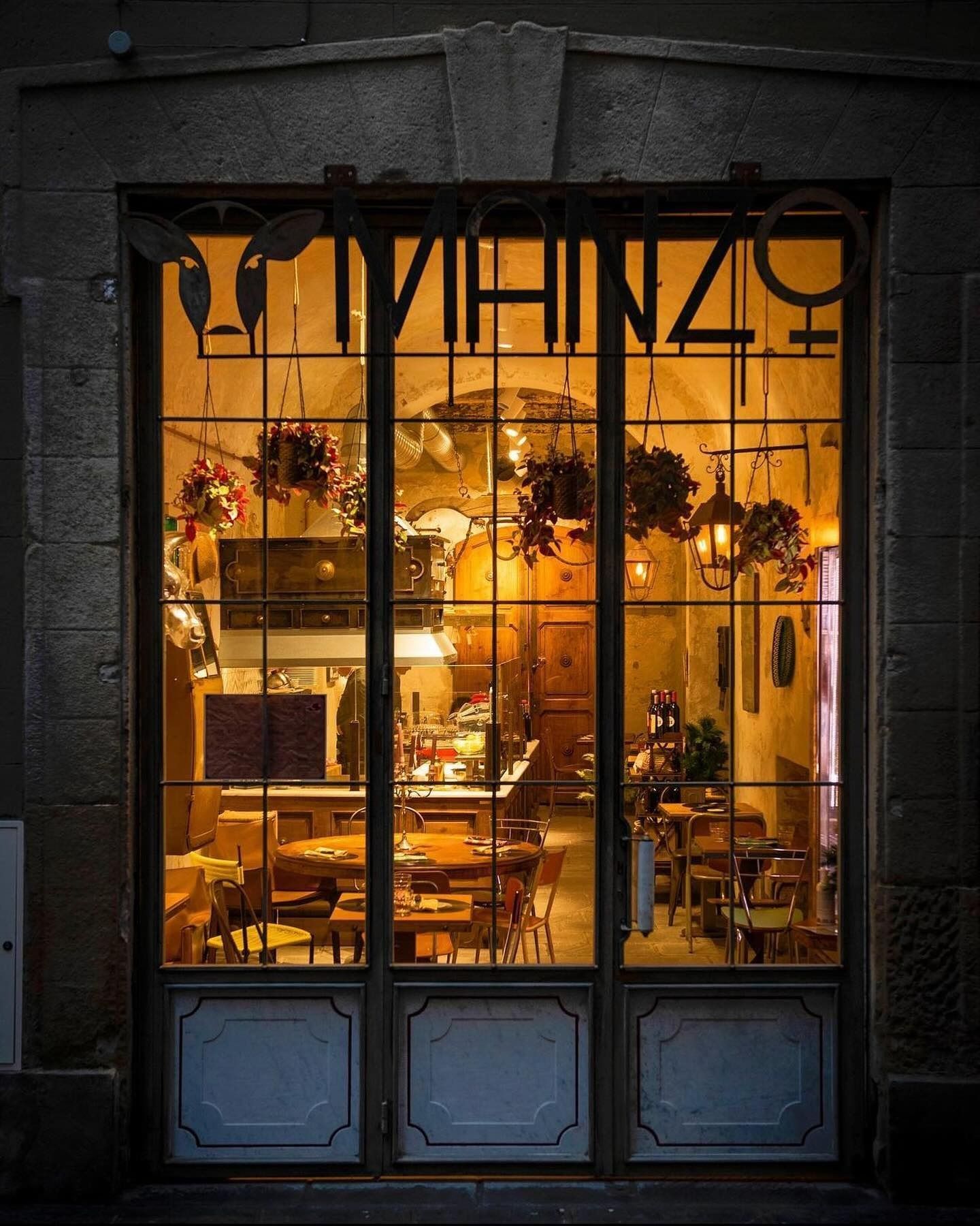Interno del bar illuminato attraverso porte in vetro con piante sospese, tavoli e sedie e un'insegna con la scritta 