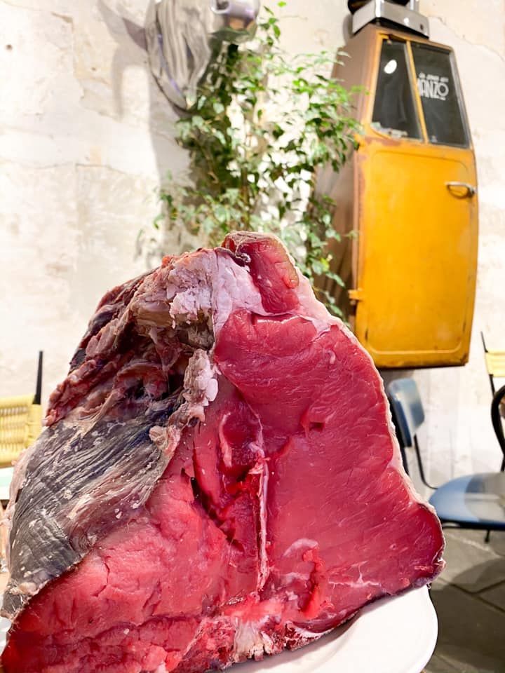 Bistecca di manzo alla fiorentina tagliata a fette e grigliata con rosmarino, servita su un tagliere di legno con una piccola ciotola di sale.