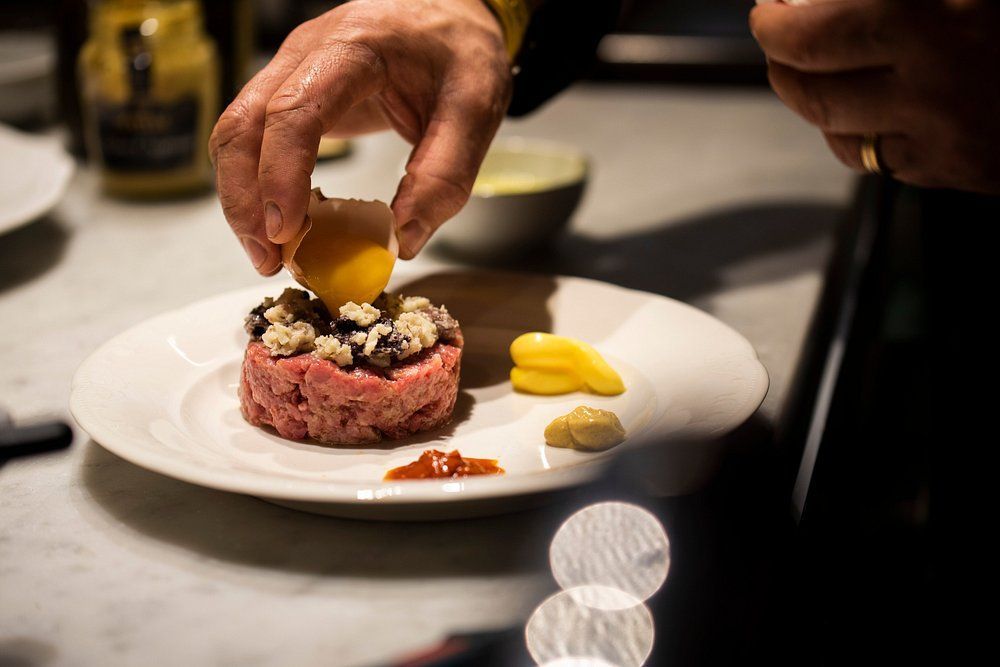 Disporre a mano il tuorlo d'uovo su una tartare di manzo, guarnita con funghi, su un piatto, con salsa e condimenti.