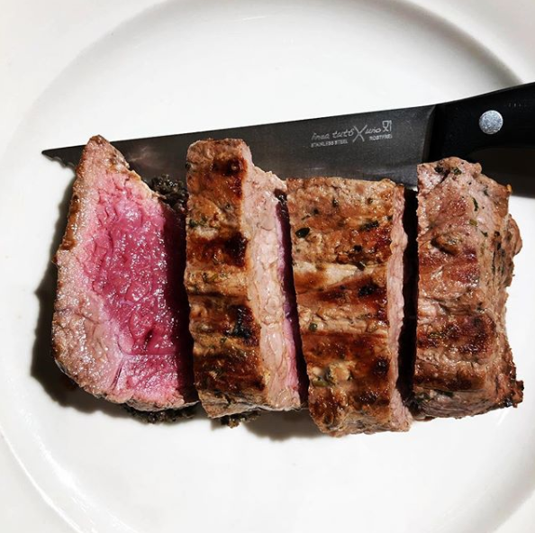 Persona con guanti blu che pesa carne cruda su una vecchia bilancia in cucina.