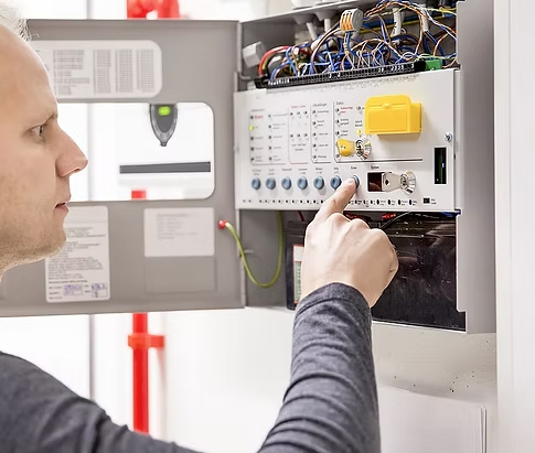 A person adjusting a fire alarm control panel inside a white cabinet, with a finger touching a button on the interface.