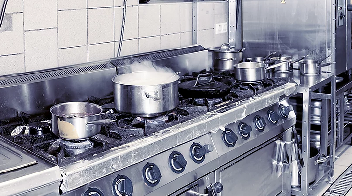 A stainless steel commercial stove in a tiled kitchen, featuring pots on burners with steam rising from one.
