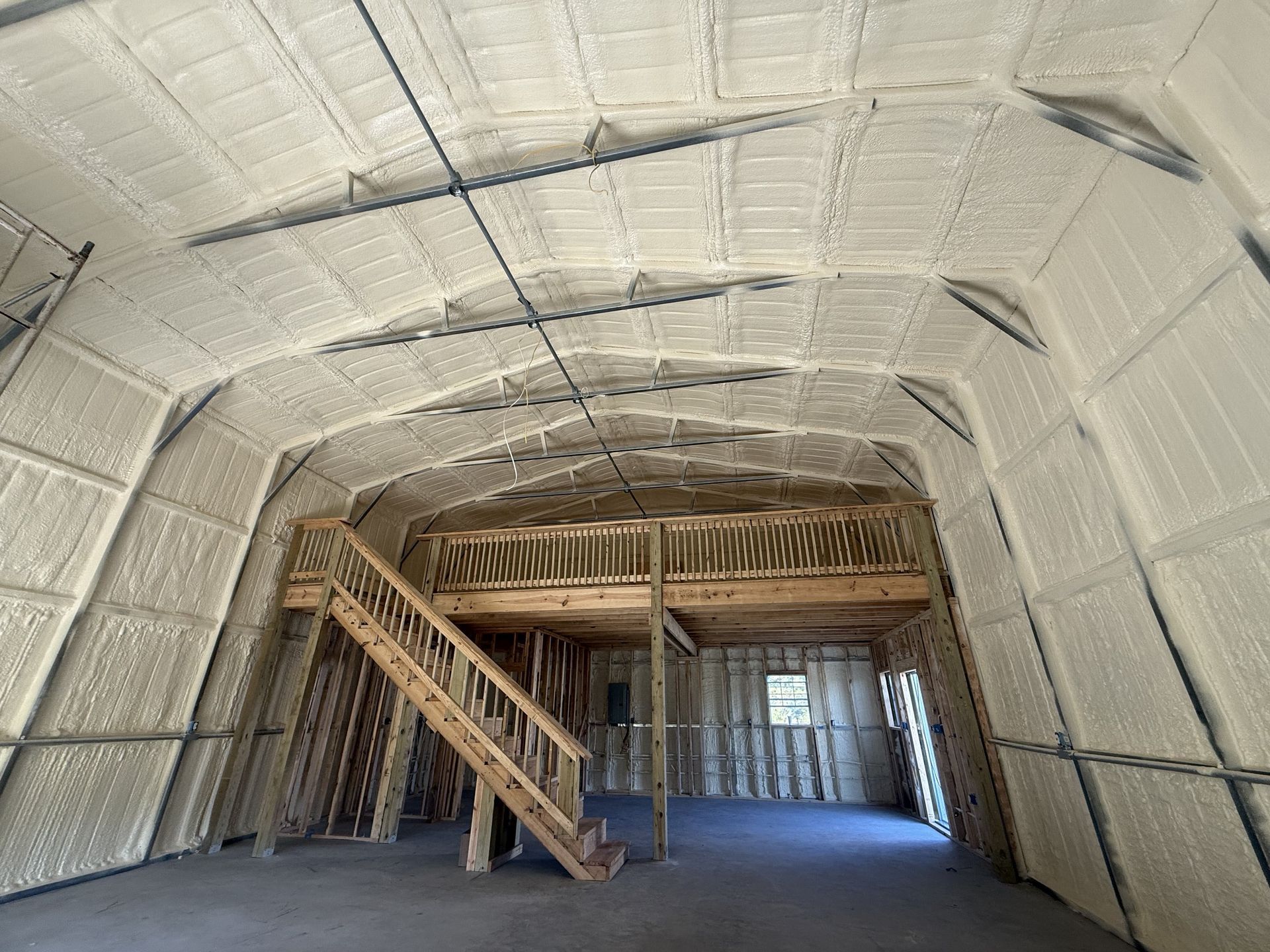 Interior of a building with foam insulation on the walls and ceiling. A wooden loft and stairs are visible.