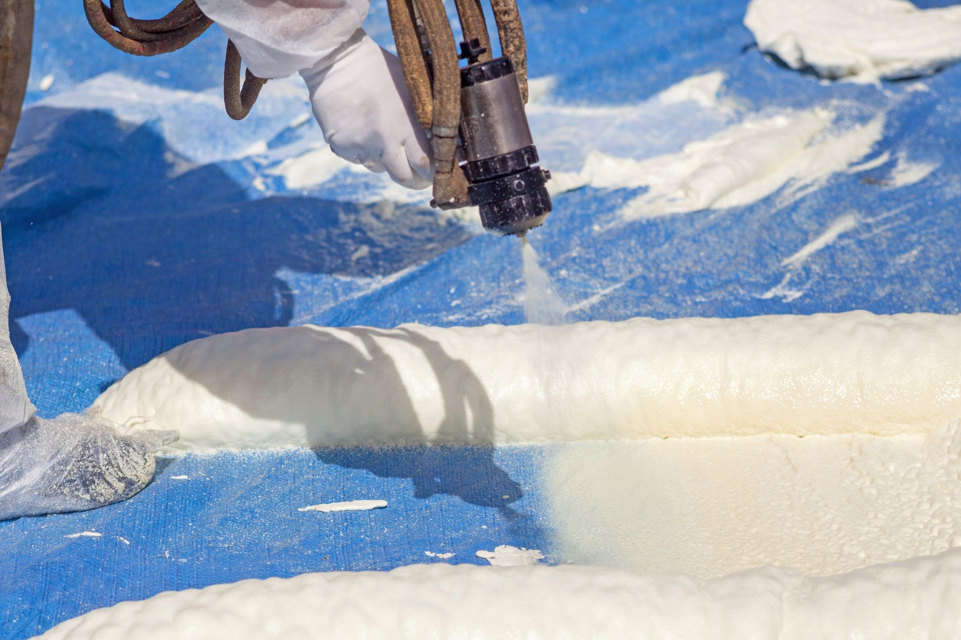Person spraying expanding foam insulation on blue tarp.