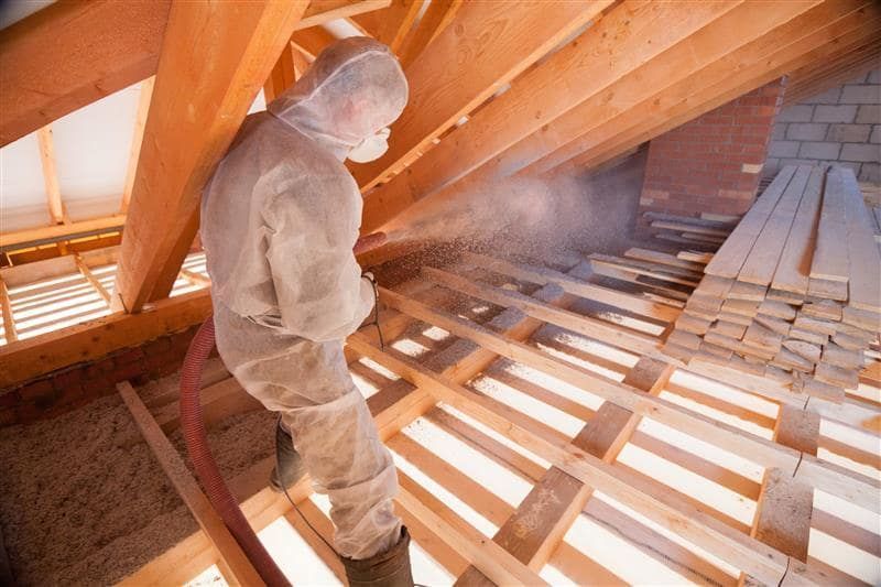 Person in protective suit spraying insulation in an attic.