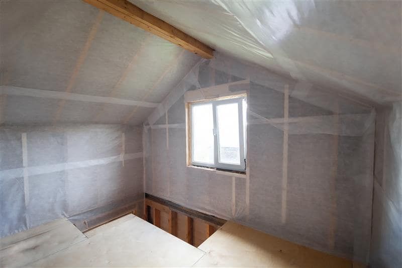 Interior of a room under construction, walls and ceiling covered in clear plastic sheeting, a small window.
