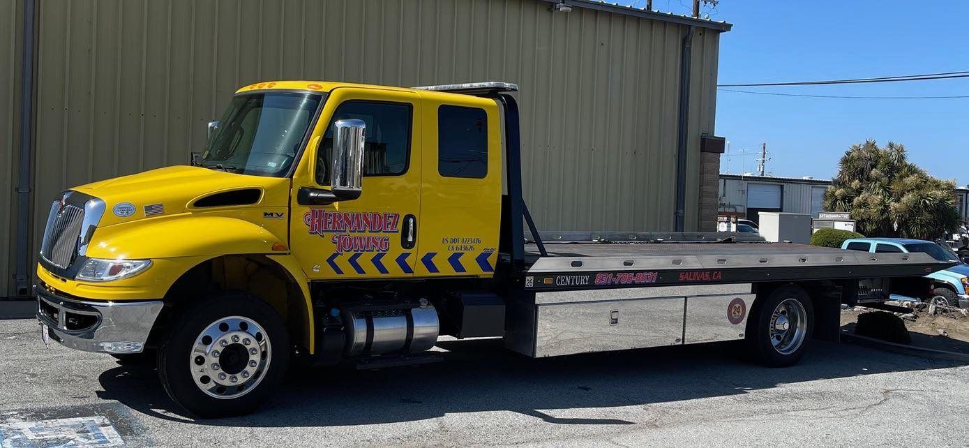 Yellow tow truck parked outside a building on a sunny day.