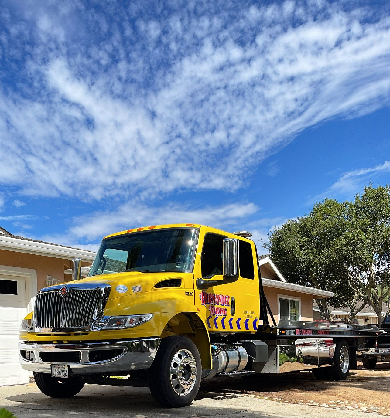 A damaged blue car being secured to a tow truck by a person in a vest.