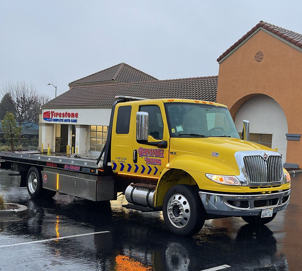 Damaged white van loaded on a tow truck by a person in an orange vest on a city street.