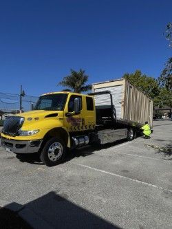 Yellow tow truck transporting a tan storage container on a sunny day.