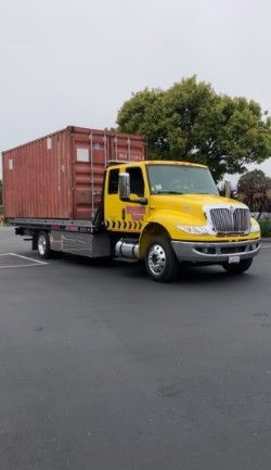 Yellow flatbed truck transporting a red shipping container on an asphalt surface.