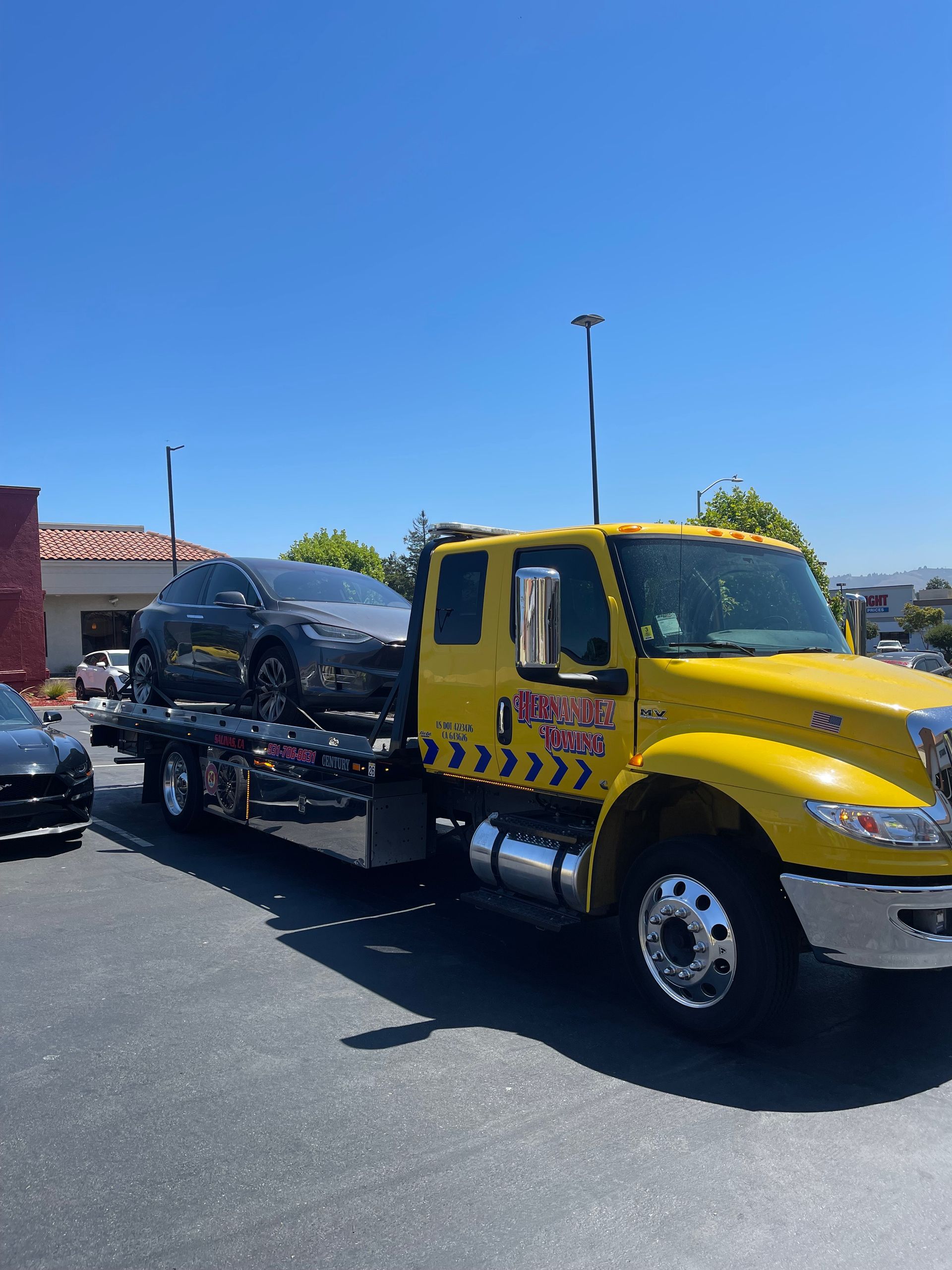 Yellow tow truck carrying a gray car on a sunny day.