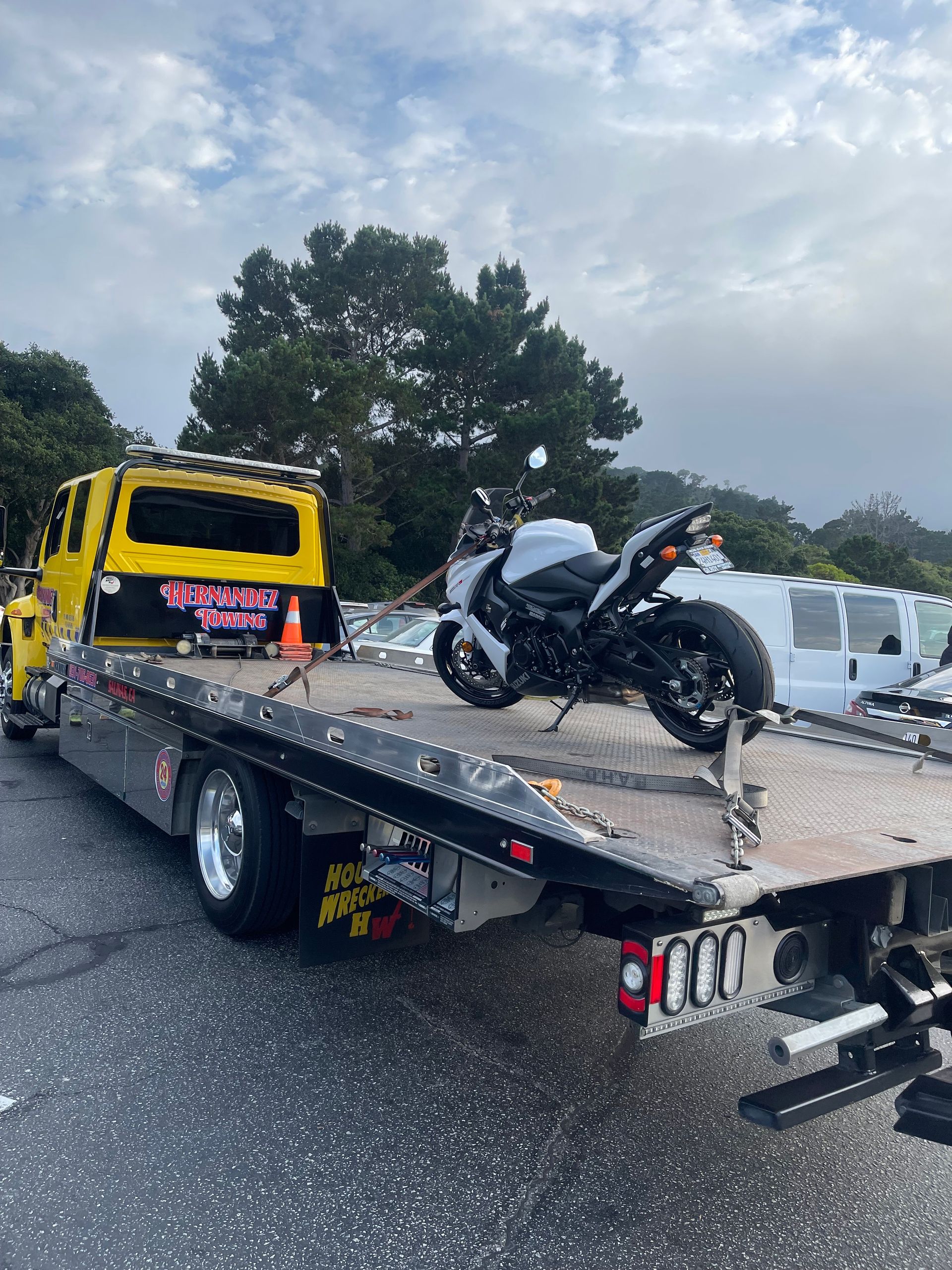 Motorcycle on a yellow tow truck bed, likely being transported. Outdoors, overcast.