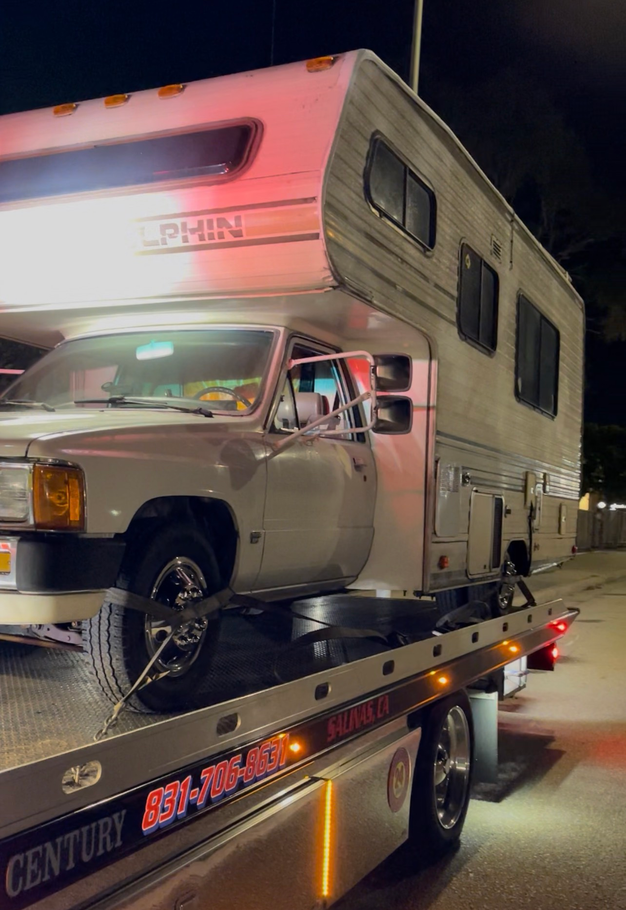 A white van with front-end damage being loaded onto a tow truck on a road. A white van with front-end damage being loaded onto a tow truck on a road.